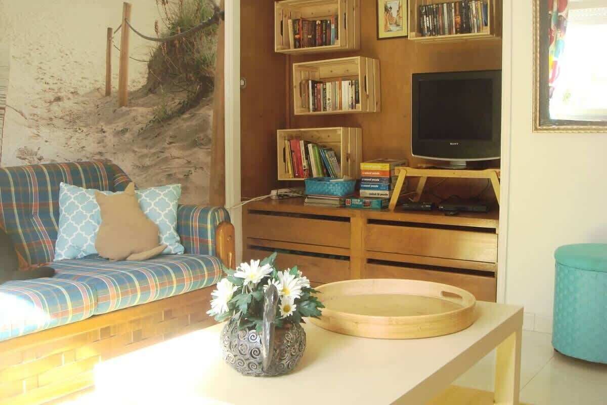 Una sala de estar con un sofá, una mesa de centro con un jarrón, una estantería, un televisor y una mesita redonda.
