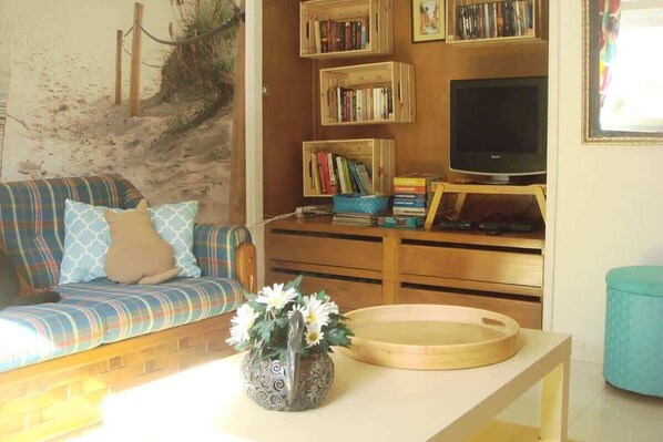 A living room with a sofa, a coffee table with a vase, a bookshelf, a television, and a small round table.