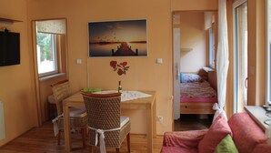 Ett rum med ett träbord, flätade stolar, en säng och en målning som föreställer en solnedgång.