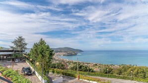 Une vue sur la côte, avec un sentier pavé, une voiture garée et une ville lointaine au bord de la mer.