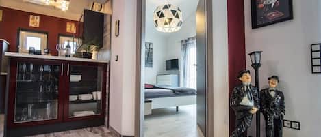 A modern interior with a wooden cabinet, a dining area, and a bedroom visible through an open doorway.