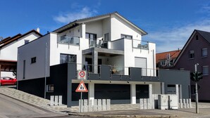 A modern two-story building with a balcony, a pedestrian crossing sign, and a speed limit sign. - Modern & TOP-equipped apartment (up to 6 pers.) + Netflix + bicycle garage (Uhldingen/Mühlhofen)