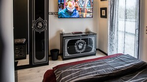 A bedroom with a bed, a TV mounted on the wall, a chandelier, and a window with curtains. - Modern & TOP-equipped apartment (up to 6 pers.) + Netflix + bicycle garage (Uhldingen/Mühlhofen)