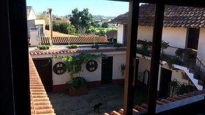 A view through a window of a courtyard with a tiled roof, a dog, and potted plants. - Caetano Rustic House - West of Portugal (Chã da Laranjeira)