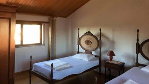 A room with two wooden beds, a small bedside table with a lamp, and a window with curtains. - Caetano Rustic House - West of Portugal (Chã da Laranjeira)