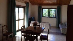 A spacious living area with a wooden ceiling, a dining table with chairs, a sofa, and a TV. - Caetano Rustic House - West of Portugal (Chã da Laranjeira)