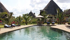 A pool area with lounge chairs and thatched-roof structures. - Stunning villa Twiga in African style with Wi-Fi (Diani Beach)