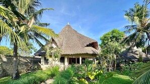 A thatched-roof house surrounded by lush greenery and palm trees. - Stunning villa Twiga in African style with Wi-Fi (Diani Beach)