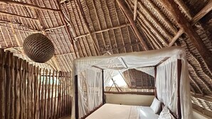 A thatched-roof room with a bed covered by a white canopy. - Stunning villa Twiga in African style with Wi-Fi (Diani Beach)