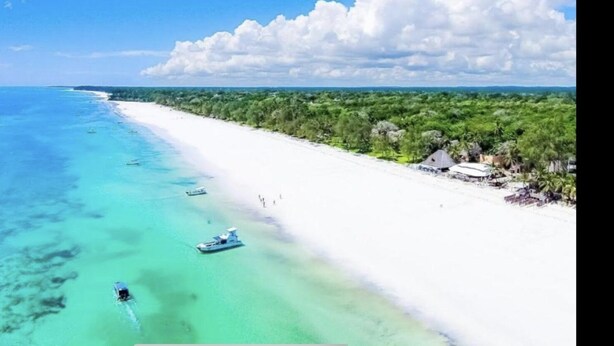 A beach with clear turquoise water, white sand, and a line of trees and buildings along the shore. - Stunning villa Twiga in African style with Wi-Fi (Diani Beach)