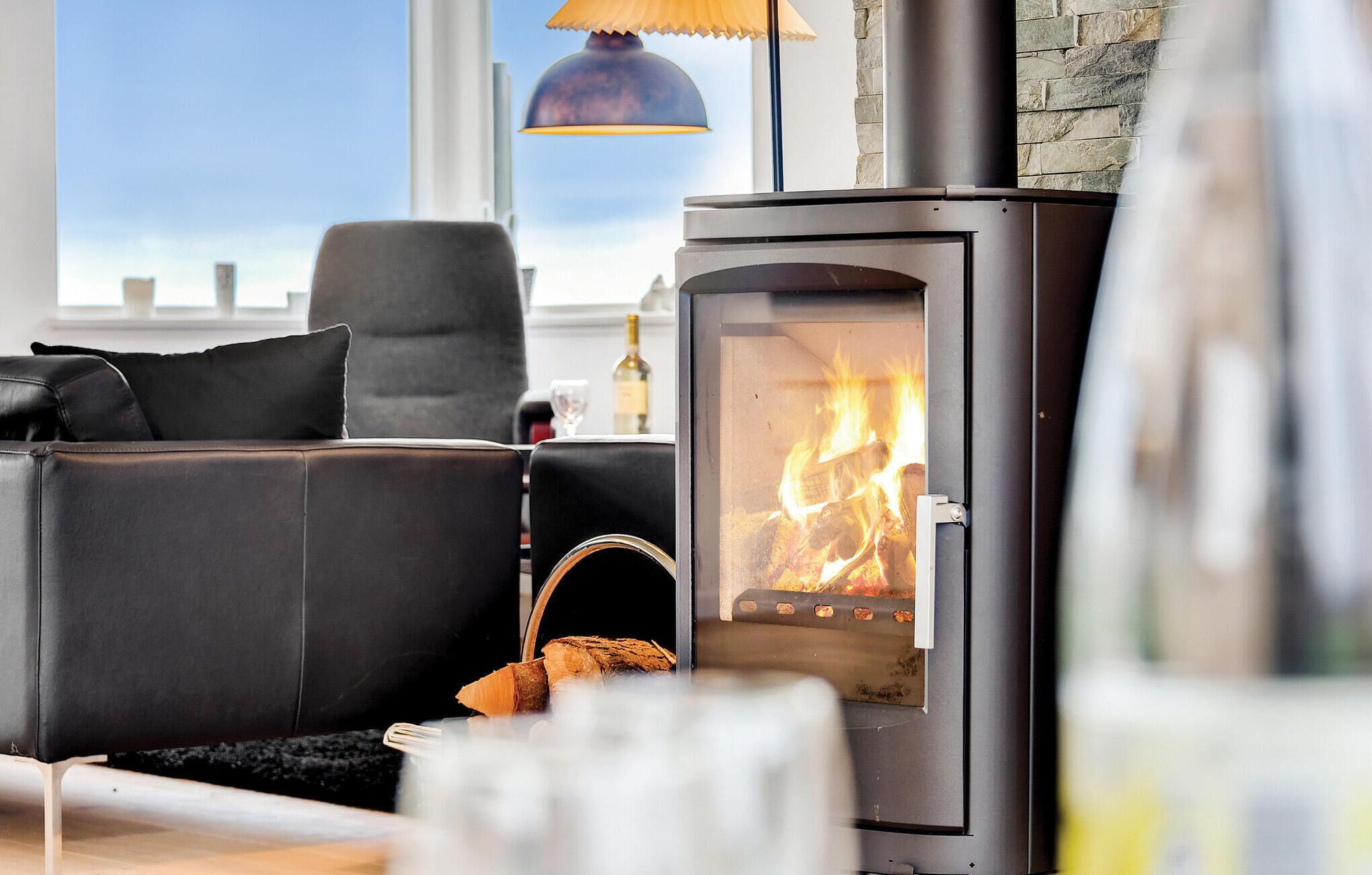 A modern living room with a black leather sofa, a glass fireplace, and a stone wall.