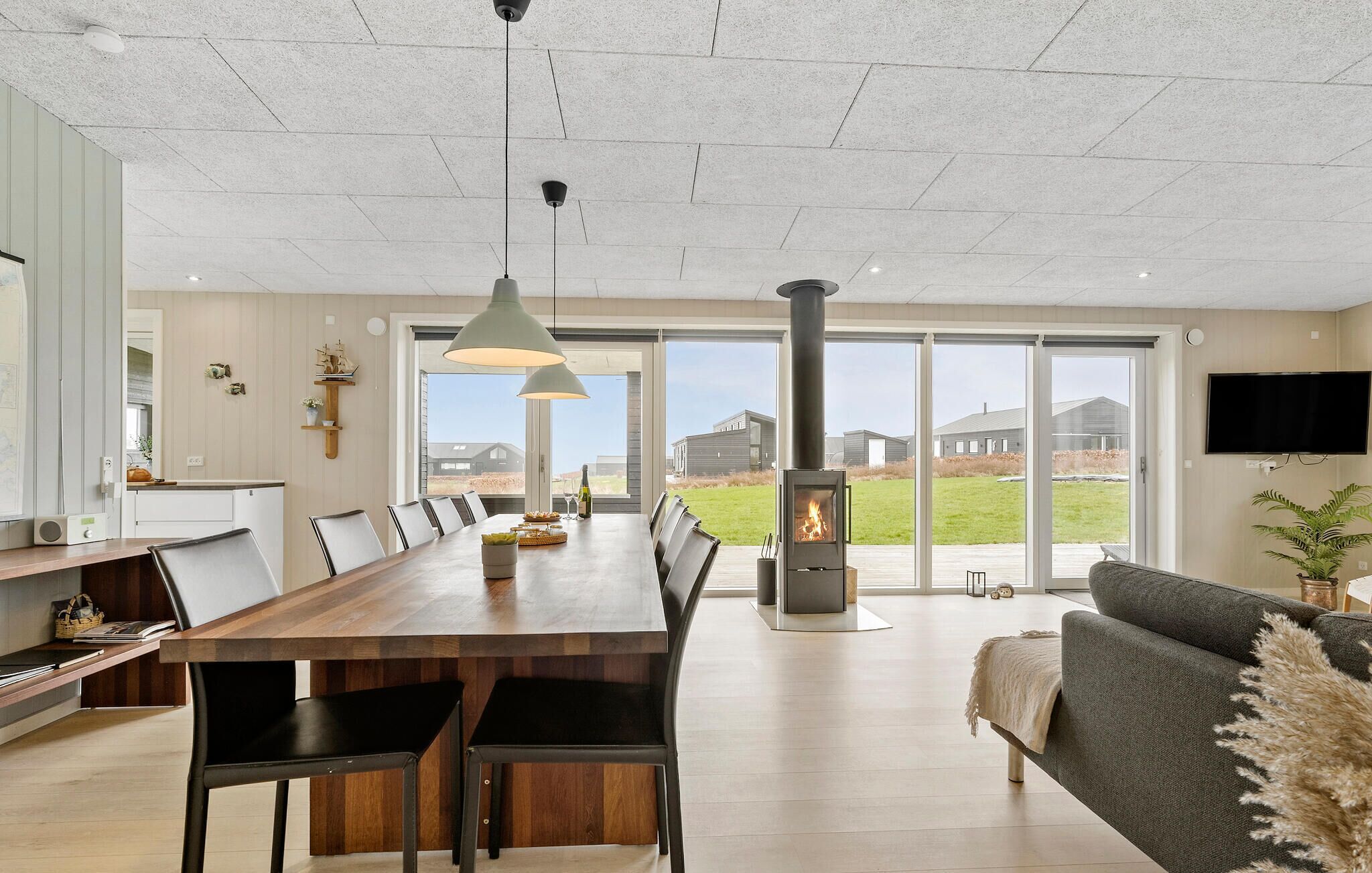 Cozinha ampla com uma grande mesa de jantar, luminárias pendentes modernas e um fogão a lenha embutido.
