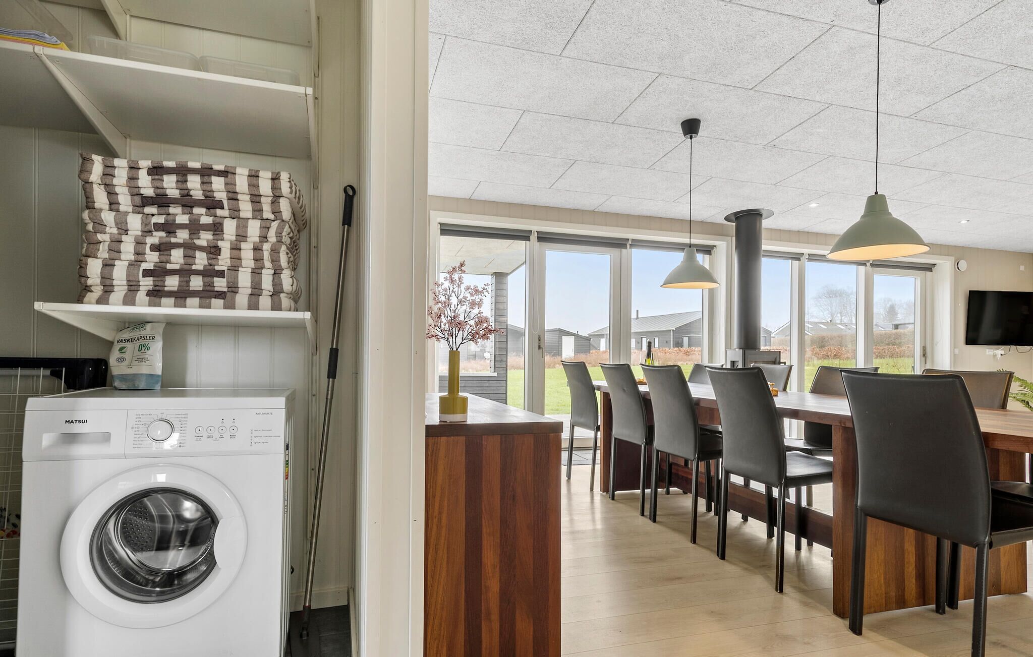 Una cocina moderna con lavadora integrada, un comedor con mesa y sillas de madera, y un ventanal que ofrece vistas al exterior.