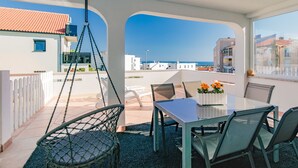 Eine Terrasse mit Tisch und Stühlen, einem Hängesessel und Blick aufs Meer.