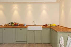 A kitchen with light green cabinets, a wooden countertop, a white sink, and various kitchen items.