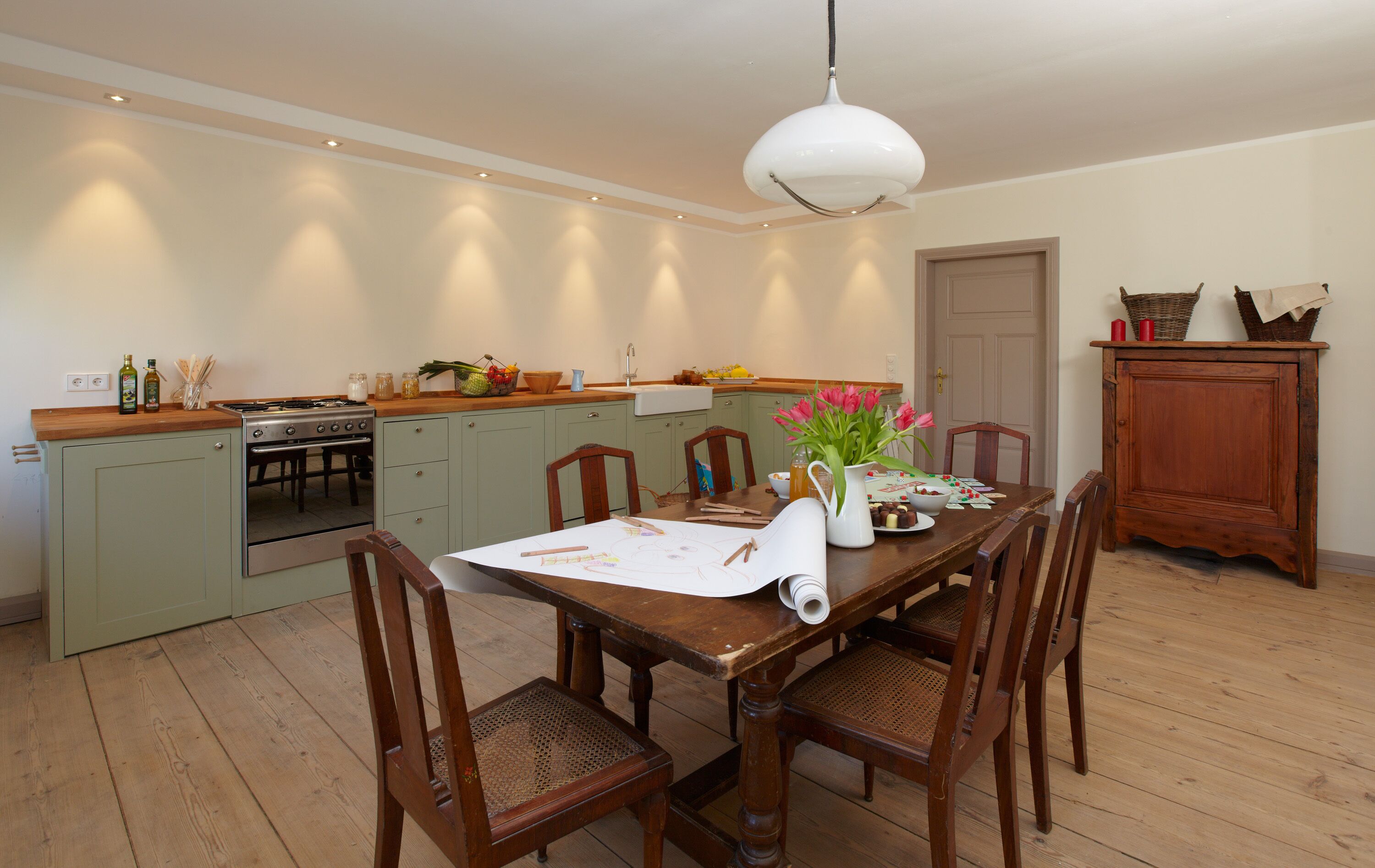 Une cuisine avec des meubles de rangement en bois, une table à manger avec des chaises et un luminaire suspendu.