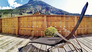 Eine Holzdielen-Terrasse mit einem Klappstuhl, einem kleinen Topfpflanze und einem Holzzaun mit rautenförmigen Ausschnitten.