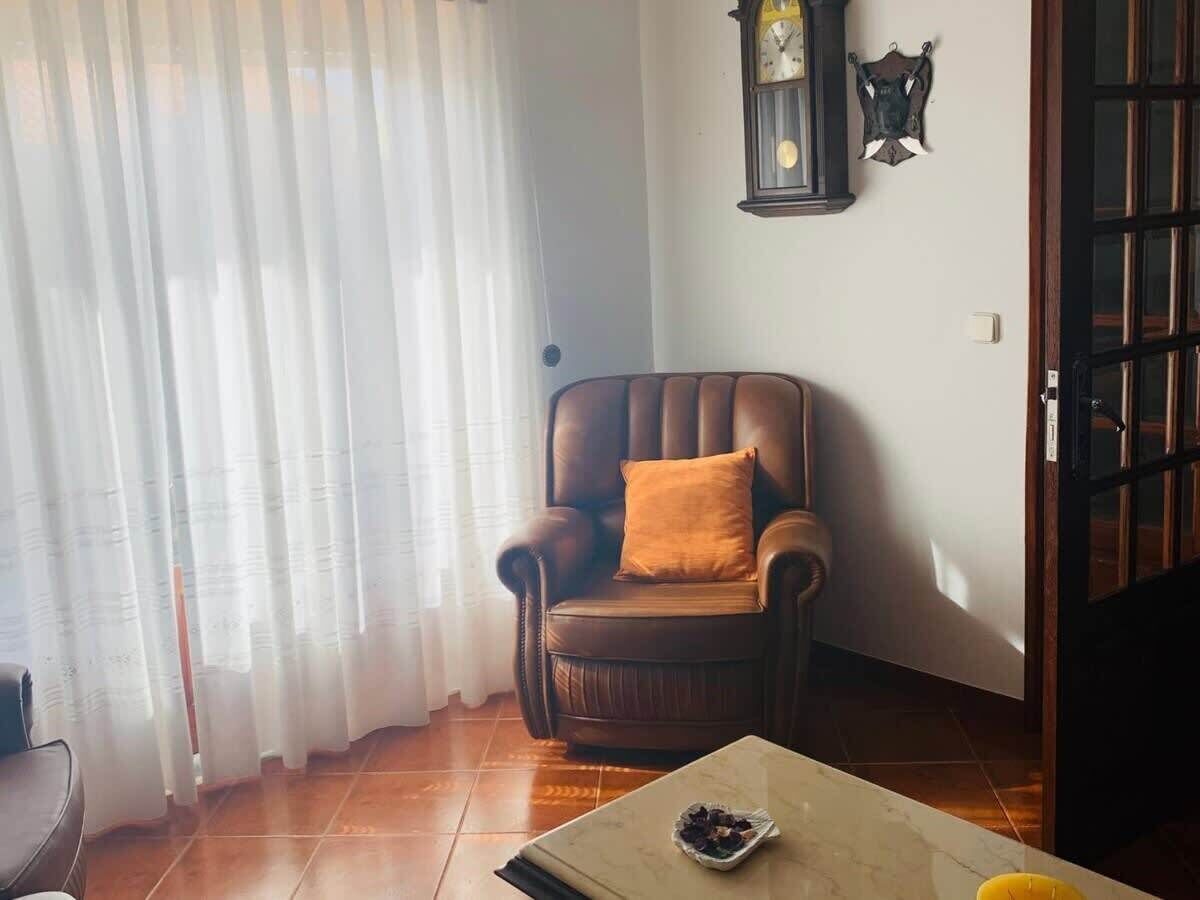 Una habitación con un sillón de cuero, una mesa con un plato de comida, un reloj y un perchero.