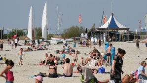 A beach with people sunbathing and swimming, a tent labeled 'Surf Chile', and sailboats in the background.