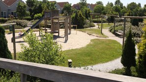 A playground with climbing structures and a slide, surrounded by a landscaped garden and residential buildings.
