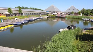 A calm water body with boats docked, a building with a pyramid-shaped roof, and a grassy area in the foreground.