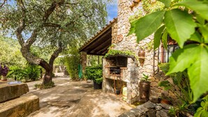 Un edificio de piedra con horno de piedra, rodeado de follaje y árboles.