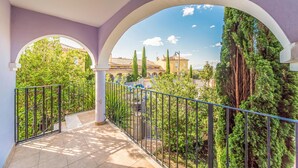 Un balcón con vistas a un patio interior, que presenta suelo de baldosas, barandillas metálicas y abundante vegetación.