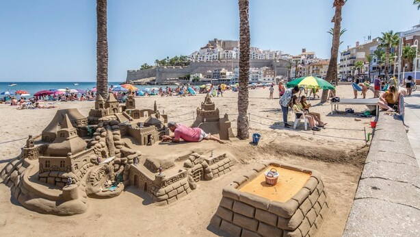 Una playa arenosa con un castillo de arena grande y palmeras.