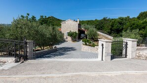 A stone building with a paved driveway leading to a gated entrance.