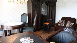 A room with a dark wooden cabinet, a round table with magazines, a leather armchair, and a floral-patterned sofa.
