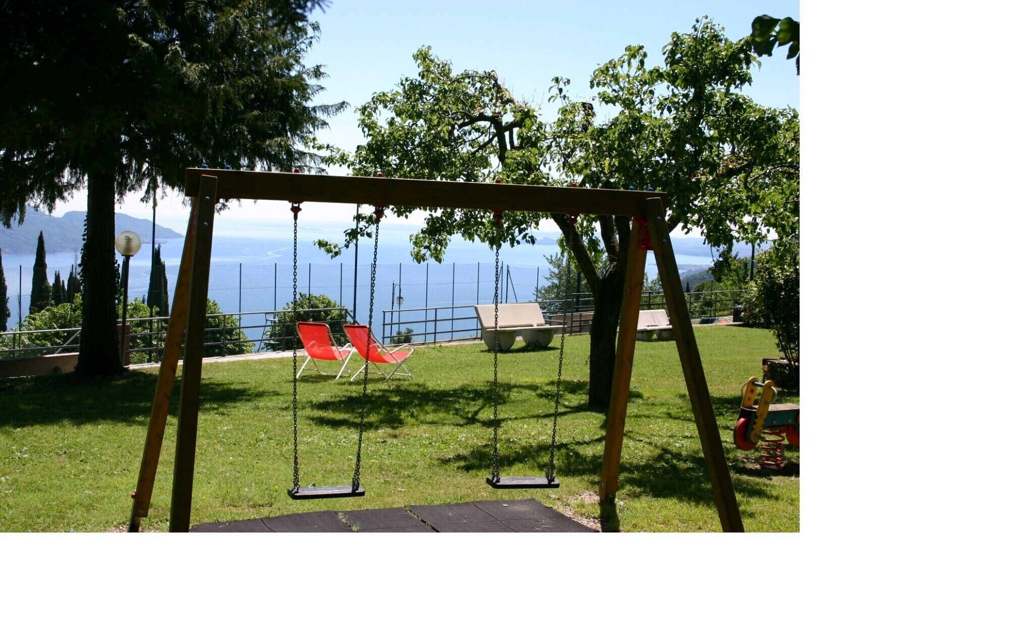 Ein hölzerner Spielplatz mit zwei Schaukeln, einer Bank und einem Blick auf einen See und Berge im Hintergrund.