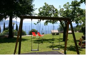Ein hölzerner Spielplatz mit zwei Schaukeln, einer Bank und einem Blick auf einen See und Berge im Hintergrund.