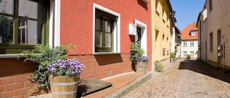 A cobblestone street with buildings on either side, featuring wooden window frames and flower pots.