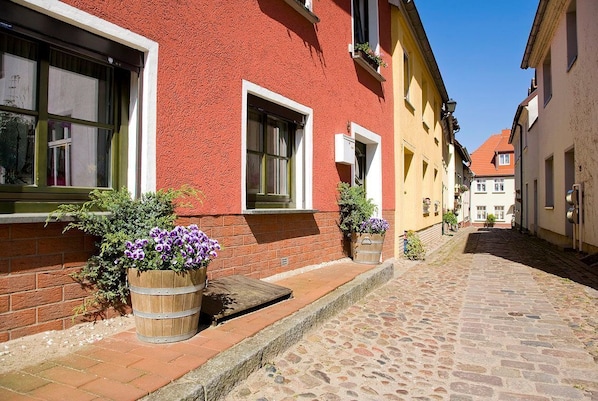 A cobblestone street with buildings on either side, featuring wooden window frames and flower pots.