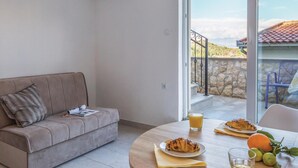 Ein modernes Wohnzimmer mit einer Couch, einem Esstisch mit Frühstücksgebäck und Blick auf eine Steinmauer und Berge.