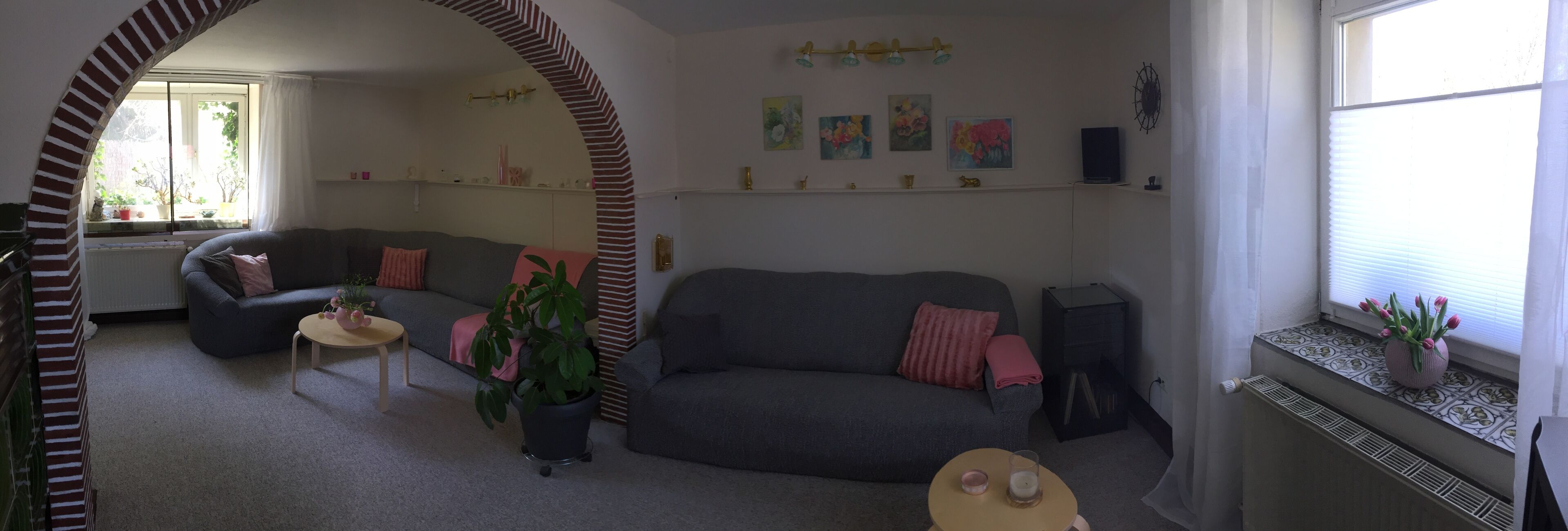 A living room with a grey sofa, a small round table, a potted plant, and a window with a view of the outdoors.