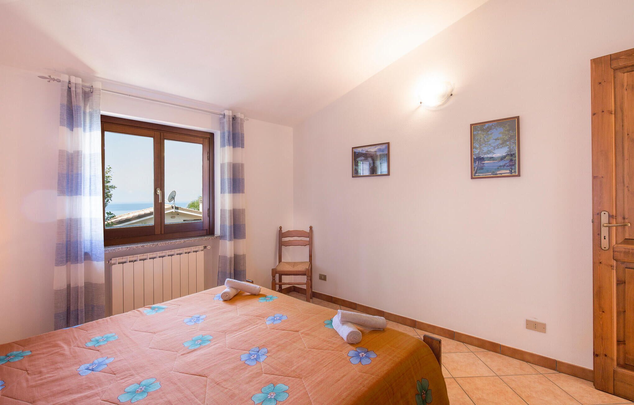 Un dormitorio con cama, una silla, un ventanal y una puerta.