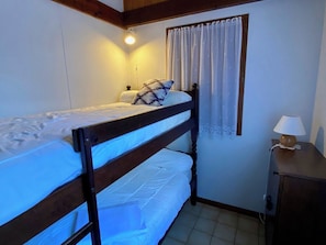 A bunk bed with a headboard, a bedside table with a lamp, a window with curtains, and a wall-mounted light.