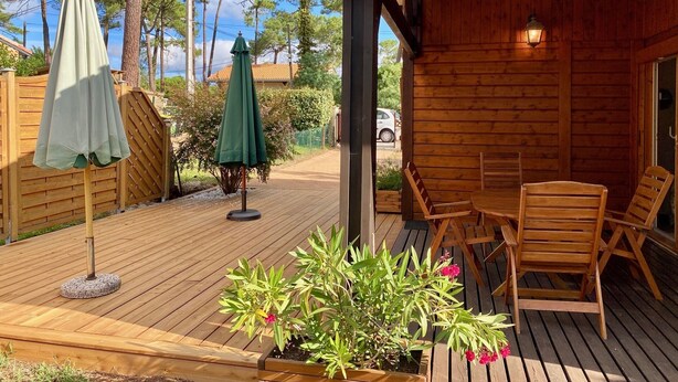 Une terrasse en bois avec des meubles d’extérieur, un espace salon couvert et une structure de cabane en bois.