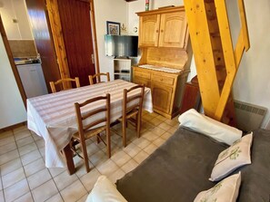 A dining area with a table and chairs, a kitchen with wooden cabinets, and a sofa with cushions.