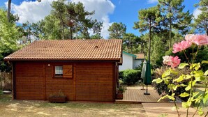 Une cabane en bois avec un toit en tuiles, entourée d’un jardin agrémenté de plantes fleuries et d’une pelouse.