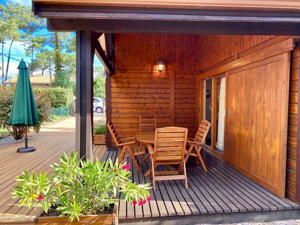 A wooden deck with a table and chairs, surrounded by plants and a green umbrella.