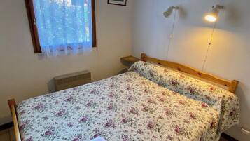 A bedroom with a bed, a window with a curtain, a wall-mounted light fixture, and a picture on the wall.