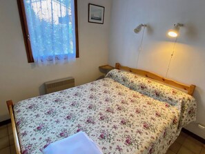 A bedroom with a bed, a window with a curtain, a wall-mounted light fixture, and a picture on the wall.