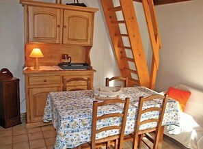 Un comedor con una mesa dispuesta para cuatro personas, sillas de madera, un armario y una escalera apoyada en la pared.