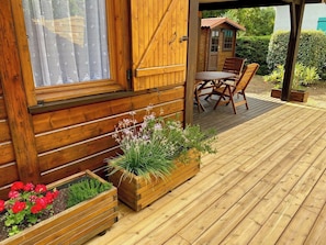 A wooden deck with a table and chairs, wooden planters with flowers, and a wooden building with a window.