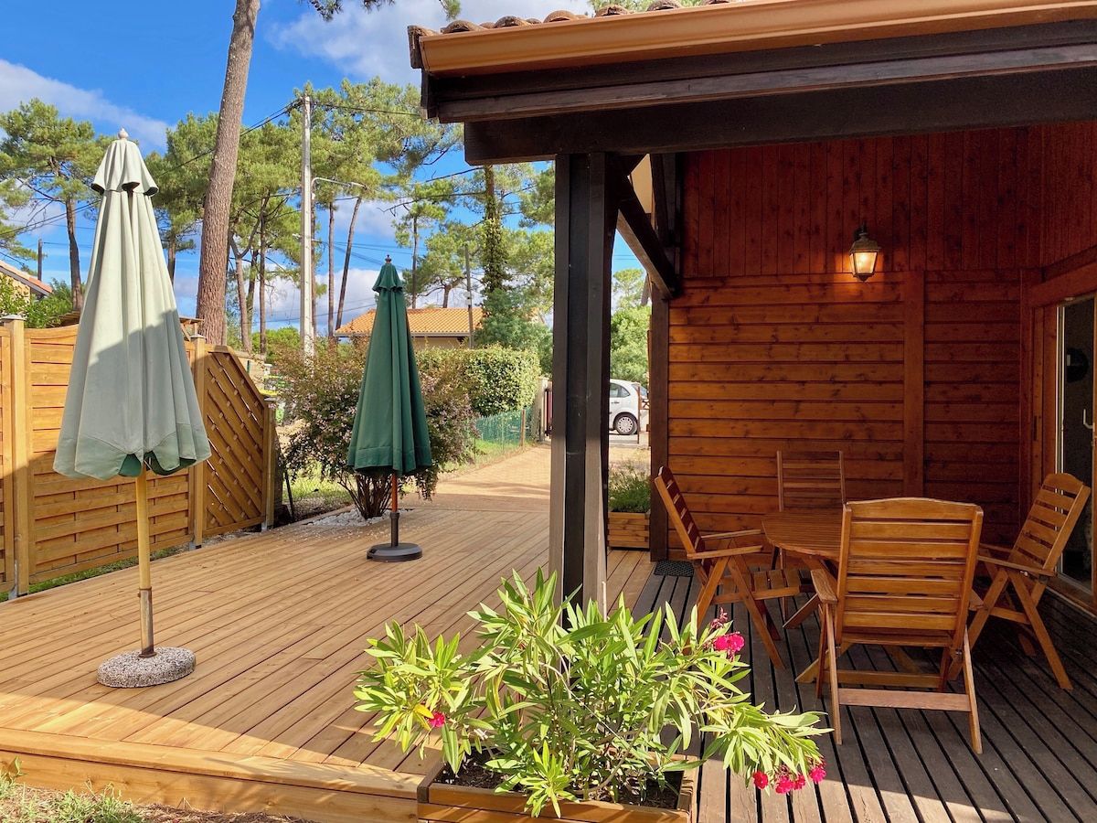 Terraza de madera con mobiliario exterior y sombrillas, rodeada por un cerco de madera y árboles.