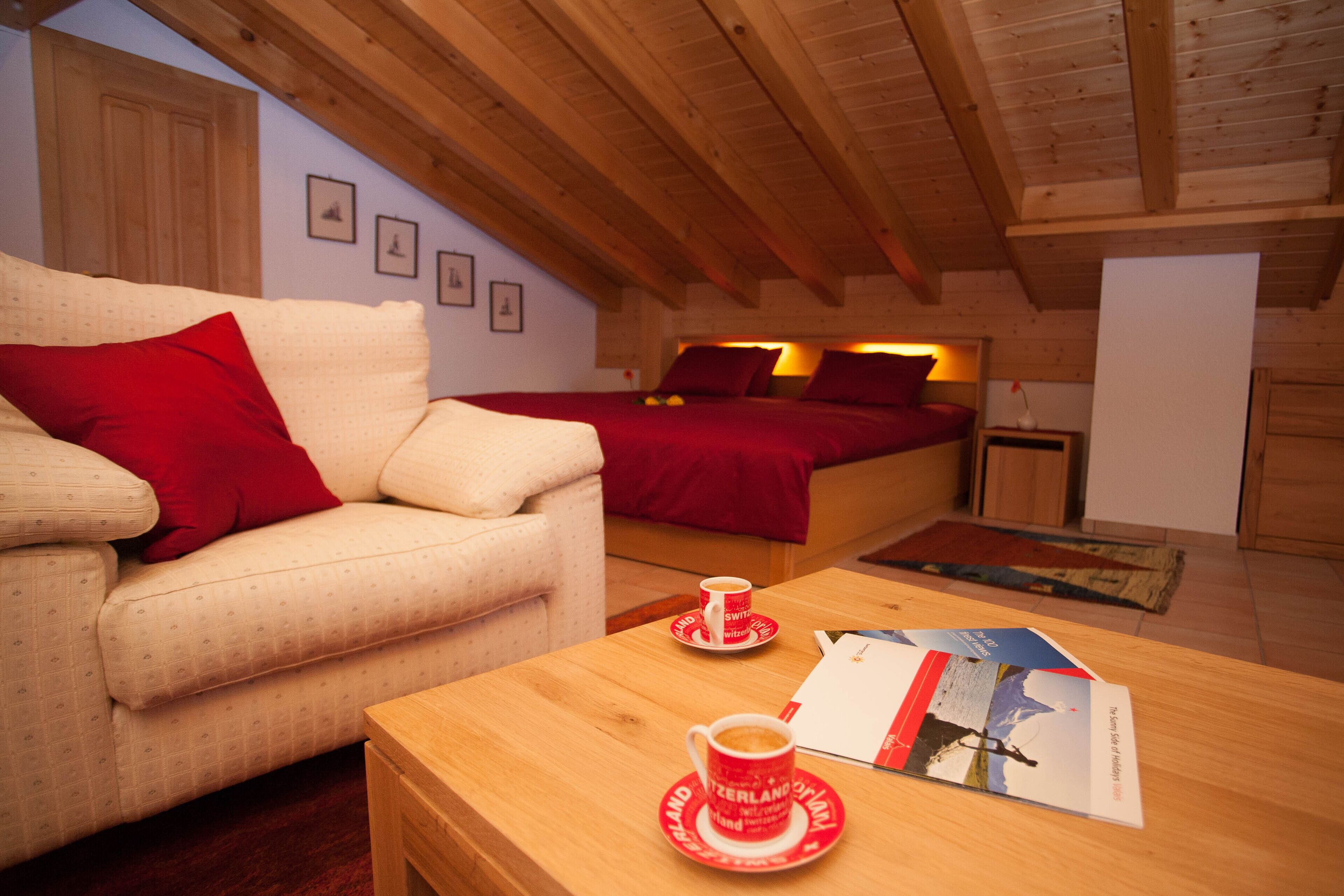 A cozy room with a sofa, a bed, a wooden table with a cup and a brochure, and a wooden ceiling.
