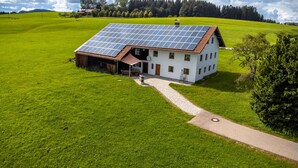 Una casa de campo blanca con techo de paneles solares, rodeada de campos verdes exuberantes y un cielo despejado.
