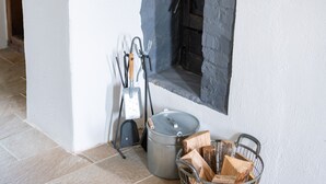 Una chimenea de piedra con un soporte de metal para leña y una cesta de metal llena de leña.